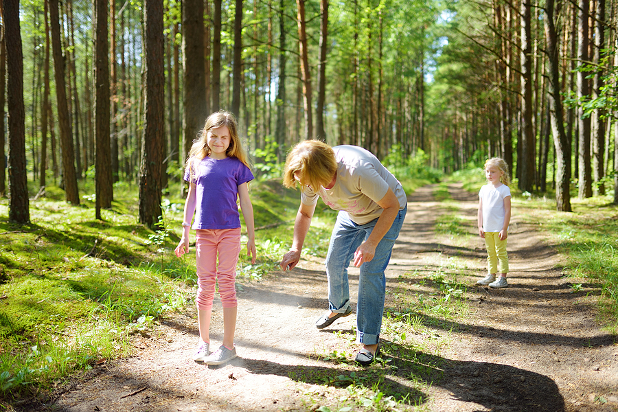 Middle age woman applying insect repellent to her granddaughter before forest hike beautiful summer day. Protecting children from biting insects at summer. Active leisure with kids.